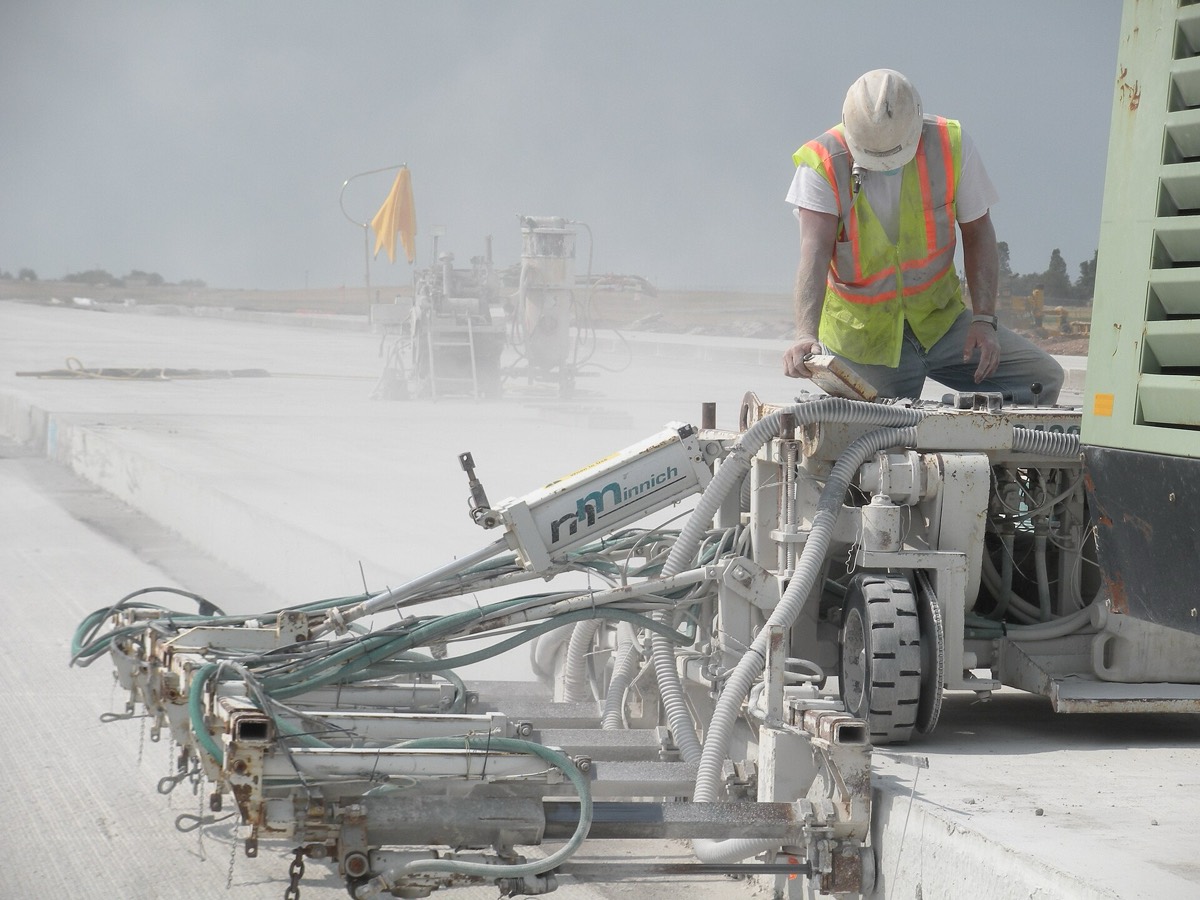 A construction worker operating drilling equipment on a runway on a hot day