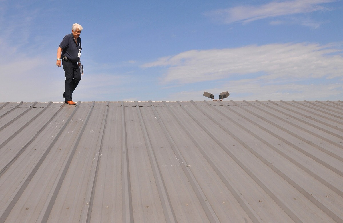 An inspector walking across a damaged commercial roof under a blue sky
